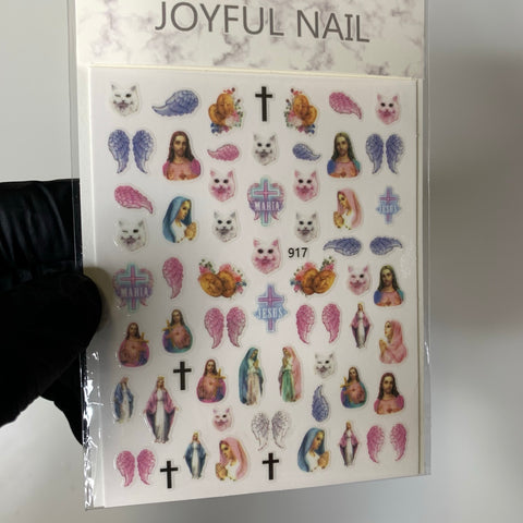 A sheet of religious-themed stickers for nail art design includes detailed and colorful images such as angels, Mary, crosses, wings, and small animals on a white background. The sheet, held by a gloved hand at the edge, is labeled Dynamic Nail Supply's Religion Stickers - Angels - Mary Saint Sticker.