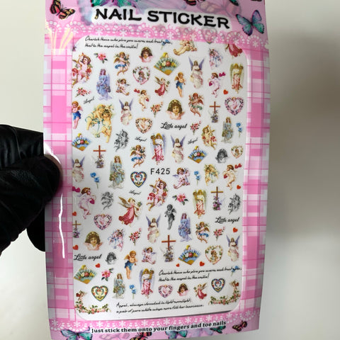 A package of Religion Stickers for nail art by Dynamic Nail Supply features a pink plaid border and includes an assortment of designs such as angels, crosses, hearts, and floral elements. Some stickers are labeled "Little Angel," reflecting the charm associated with religious motifs. A gloved hand presents the package against a simple white background.