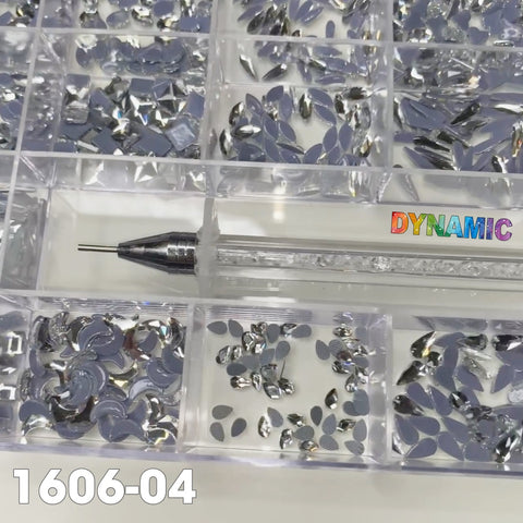 A clear compartmentalized box containing 1000 Silver Crystal Rhinestones, designed for nail art with 20 different shapes, is topped with a DYNAMIC brand picker pen in vibrant lettering. The box features the SKU: 1606-04 in the bottom left corner.