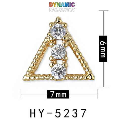 Elevate your manicure with this luxurious jewelry-inspired nail art design by Dynamic Nail Supply. This gold triangular nail decoration, adorned with three clear gemstones in a vertical arrangement, measures 7mm wide and 6mm tall—perfect for adding a touch of elegance to your nails. Labeled with "Dynamic Nail Supply" above and "HY-5237" below, this piece seamlessly blends opulence and style.