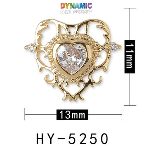 This opulent heart-shaped nail art charm, a part of the Luxurious Jewelry for Nail Art design collection by Dynamic Nail Supply, is adorned with a central clear gemstone and intricate gold detailing. It measures 13mm by 11mm and bears the model number HY-5250. "Dynamic Nail Supply" is prominently showcased above the charm in vibrant lettering.