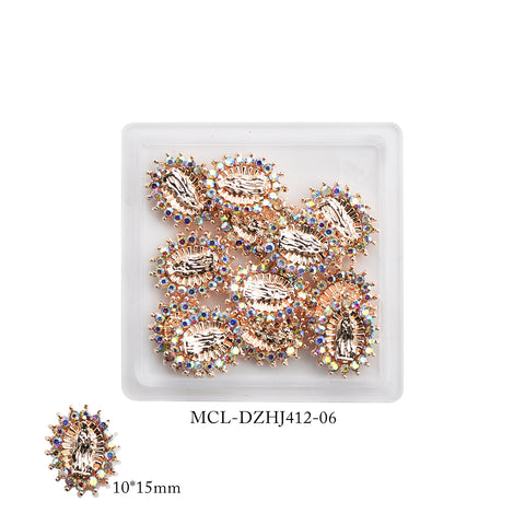 A small, square white tray displays a set of intricate, oval-shaped Virgin Mary charms from Dynamic Nail Supply. These small embellishments, each highlighted by a border of iridescent gems, add religious elegance to nail designs. One charm in the bottom left corner measures 10*15mm and is marked with the code MCL-DZHJ412-06.