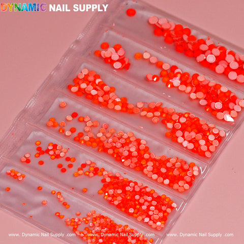 The Round-shape Mixed-sizes Neon Rhinestone set by Dynamic Nail Supply showcases red and orange round nail art sequins of various sizes, all neatly organized within a six-compartment clear plastic package. The Dynamic Nail Supply brand name is prominently displayed at the top and bottom edges against a pink background.