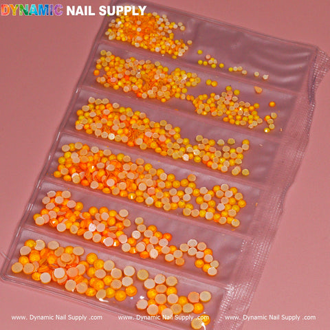 A vibrant Round-shape Mixed-sizes Neon Rhinestone set is housed in a plastic organizer with eight compartments, containing small neon rhinestones in various shades of yellow and orange. The logo "Dynamic Nail Supply" is displayed in colorful letters on the top left corner. This eye-catching set sits on a muted pink surface.