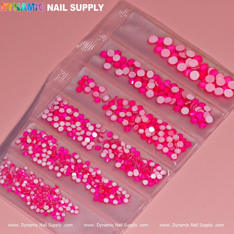A transparent plastic bag contains multiple compartments filled with circular nail art embellishments in shades ranging from light pink to fuchsia, including a striking neon rhinestone set to add a bold touch. The top left corner features the brand name "Dynamic Nail Supply" in colorful letters against a soft pink background.