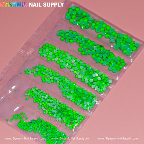 A plastic pouch with eight clear compartments displays the Round-shape Mixed-sizes Neon Rhinestone set, showcasing bright neon green nail art sequins of various sizes. Positioned against a pink background, "Dynamic Nail Supply" is printed in colorful letters at the top left corner.