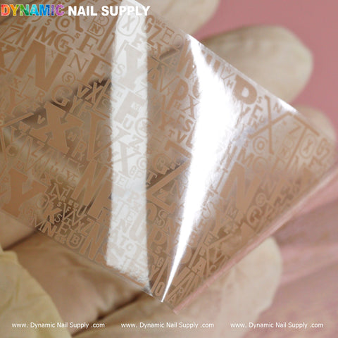 The image showcases a close-up of the Nail Art Design Foils - Letters Style from Dynamic Nail Supply, featuring delicate metallic letters in various fonts and sizes. The sheet glistens with a shiny transparency against a soft pink background, while the foils reflect light to create a glossy effect, complete with "Dynamic Nail Supply" repeating along the bottom edge. Perfect for nail art enthusiasts!