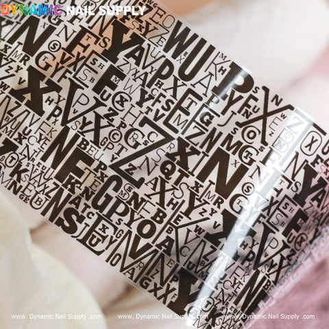 The image features a detailed shot of the Nail Art Design Foils - Letters Style by Dynamic Nail Supply, which looks like elaborate nail art with transparent layers and a mix of overlapping black alphabets. The soft pink background accentuates the stylish design, highlighting uppercase and lowercase letters in different fonts and sizes intricately covering the surface.