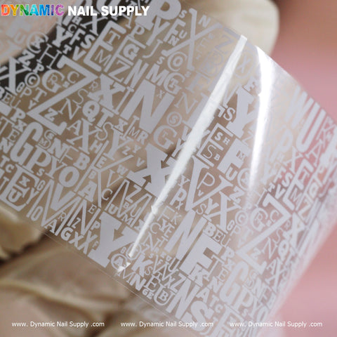 A close-up of our "Nail Art Design Foils - Letters Style" from Dynamic Nail Supply showcases a translucent sheet embellished with a variety of white letters in diverse fonts and sizes, overlapping to create a distinctive look. Set against a soft pinkish background, the playful design is highlighted, with the brand name "Dynamic Nail Supply" prominently displayed at the top in vibrant colors.