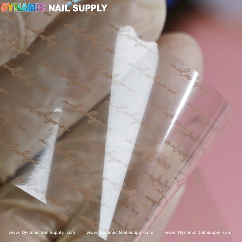 Close-up of a clear nail foil from Dynamic Nail Supply’s Nail Art Design Foils - Letters Style, showcasing cursive text reading “nailogic” in a stylish diagonal pattern. It is held by a hand in a beige glove against a pinkish background, with the brand's vibrant logo displayed in the top left corner.