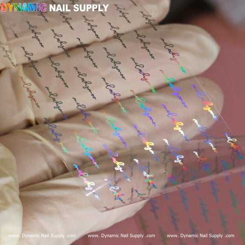 A person wearing gloves holds a transparent sheet of "Nail Art Design Foils - Letters Style" from Dynamic Nail Supply. The sheet features holographic, cursive text with the word 'hope' repeated elegantly. The soft pink background enhances the rainbow effect created by the colorful reflection of the foil, while Dynamic Nail Supply is prominently displayed at the top in multicolored text.