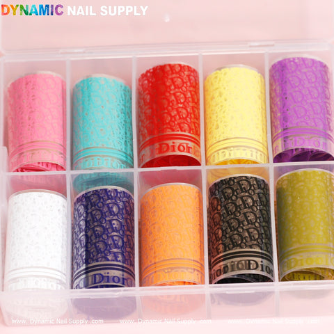 The Nail Art Design Foils - Luxury Style by Dynamic Nail Supply is a sophisticated organizer box featuring twelve compartments, each containing a roll of decorative foil in lively colors such as pink, light blue, orange, red, yellow, purple, white, blue, brown, black, gray, and gold. Each roll showcases a repetitive Dior pattern ideal for crafting eye-catching nail art designs.