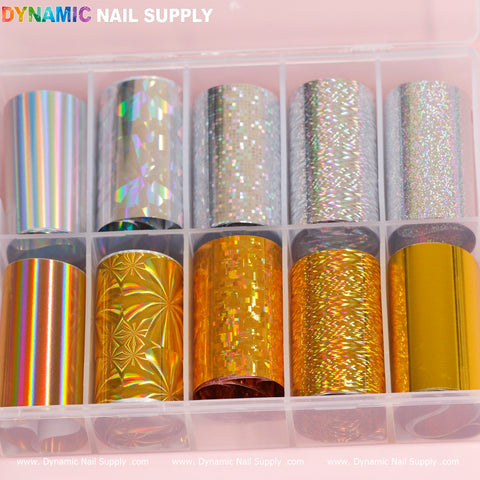 The "Nail Art Design Foils - Gold/Silver Holographic" collection from Dynamic Nail Supply features a plastic box containing ten rolls of holographic nail art foils. The top row presents iridescent silver designs, while the bottom row highlights vibrant gold patterns with a mix of geometric and abstract styles.