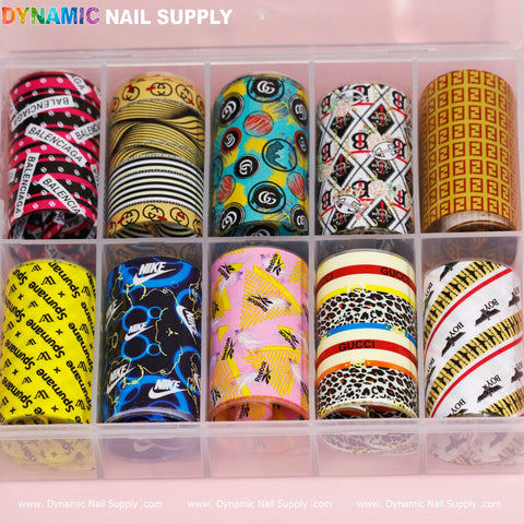 A clear organizer stylishly accommodates twelve rolls of the Nail Art Design Foils - Luxury Style by Dynamic Nail Supply. The collection features diverse designs, including pink with text, gold spiral, black logos, red and green motifs, brown checks, yellow with logos, black with blue accents, pastel triangles, leopard print, among others.