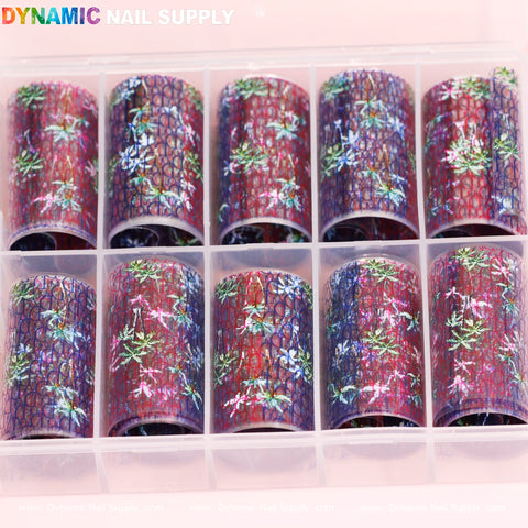 A collection of ten Nail Art Design Foils - Luxury Style, featuring vibrant floral patterns and blue lace overlays, is neatly arranged in a transparent plastic box. This set, ideal for nail art enthusiasts, comes in packaging adorned with the brand name Dynamic Nail Supply in colorful lettering across the top.