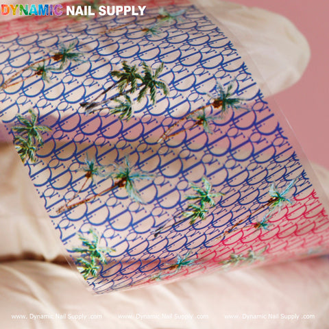 A nail art design foil from Dynamic Nail Supply features a luxury style, highlighting a tropical motif with palm trees set against a gradient pink and blue background. Accentuated by a fishnet pattern, the brand name "DYNAMIC NAIL SUPPLY" is prominently displayed at the top, while "www.DynamicNailSupply.com" is repeated along the bottom edge.