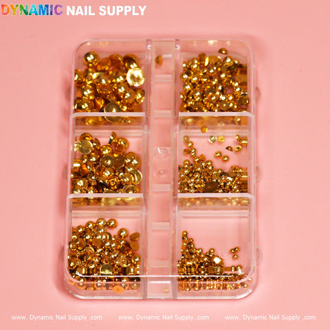 A plastic organizer box with eight compartments contains the Gold Metallic Ball Beads for Nails Design, along with rhinestones and pearls. The soft pink background complements the box labeled Dynamic Nail Supply at the top and bottom—ideal for any nails designer.