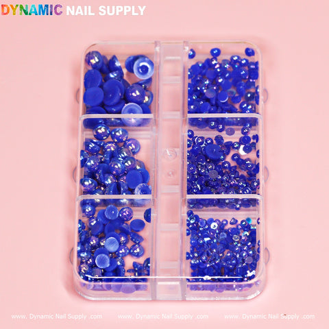 A clear plastic container from Dynamic Nail Supply, featuring six compartments each filled with round blue rhinestones of varying sizes, is perfect for nail designers. The gems sparkle against a soft pink background, with the Dynamic Nail Supply branding subtly visible at both the top and bottom.