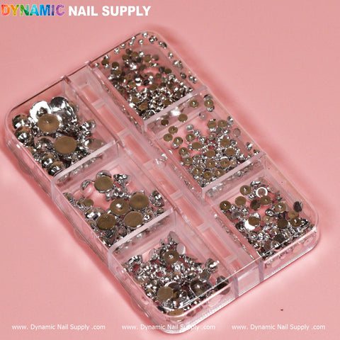 A transparent plastic organizer contains the Silver Pearl / Ball Bead for Nails Design by Dynamic Nail Supply. The organizer features eight compartments, each housing assorted silver rhinestones in various shapes and sizes. It rests on a pink surface, with the brand name "Dynamic Nail Supply" printed above it.