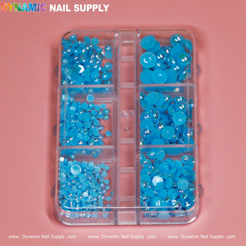 A Blue Sky Ball Bead for Nails Design, elegantly organized in a clear plastic case with nine compartments, sits on a pink surface. The assortment includes various sizes of blue rhinestones and beads, arranged from small to large, ideal for any nail designer. The Dynamic Nail Supply brand name is prominently displayed at the top and bottom of the image.