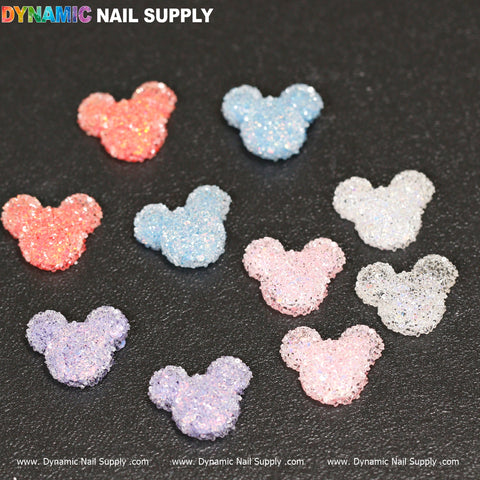 Ten shimmering Gummy/Sugar Candy Mickey Mouse Design Nail Charms are available in colors such as pink, blue, purple, and white against a black backdrop. These textured charms boast a sparkling appeal. The brand name Dynamic Nail Supply is prominently displayed at both the top and bottom of the image.