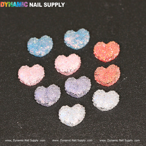 Ten pieces of Gummy/Sugar Candy Heart Shape Design Nail Charms in vibrant blue, pink, purple, and orange hues shine against a black background. These striking accents are meticulously organized in three rows under the Dynamic Nail Supply logo.