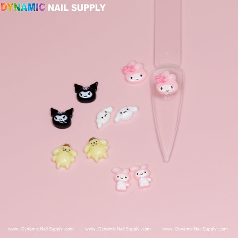 Against a pink backdrop, a clear plastic tool resembling a spoon is displayed alongside adorable nail decorations featuring small, cartoon-inspired designs such as black characters, bow-topped pink figures, ghost-like shapes, yellow bears, and pink rabbits. The DYNAMIC NAIL SUPPLY logo is prominently positioned at the top. Ideal for fans of the 10 pcs Cute Cartoon Character Design Nail Charms!