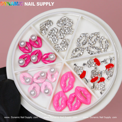 A circular nail art wheel features a variety of embellishments, including 30 pieces of 3D Lips Nail Charms from Dynamic Nail Supply. The wheel is divided into sections showcasing pearl-studded silver lips, pink lips, hot pink lips, and red-tipped silver bows. A gloved hand presents the wheel against a pink backdrop with Dynamic Nail Supply's branding prominently displayed at the top.