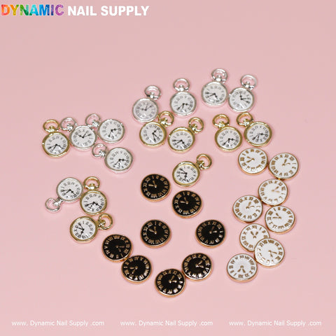 A collection of small, 3D watch face charms is displayed on a light pink background. Available in black, white, and silver with Roman numerals and gold or silver edges, these charms are perfect for nail designs. The top showcases the name Dynamic Nail Supply HQ in Houston while the bottom repeats the website: www.DynamicNailSupply.com.