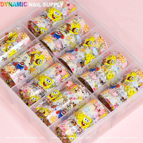 The Nail Art Design Foils - Cartoon Style by Dynamic Nail Supply come in a plastic box containing twelve rolls, each featuring colorful and vibrant cartoon-style characters, including yellow sponges and underwater themes. Each compartment holds a uniquely designed roll, and the box lid is adorned with the Dynamic Nail Supply branding in multicolored text.