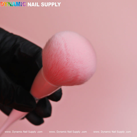 A close-up captures a hand donned in a black glove, holding a Soft-pink Dust Brush (Cosmetic-grade Duster) against a gentle pink backdrop. In the top left corner, vibrant text spells out the brand name, Dynamic Nail Supply. The image radiates cleanliness and professionalism in beauty tools.