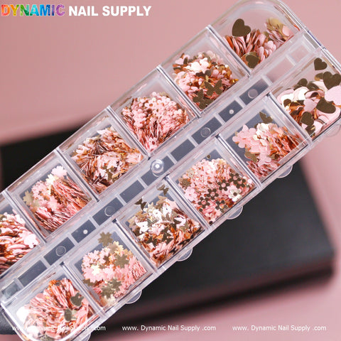 A clear, rectangular case featuring multiple compartments filled with the Pink Gold Mix-sizes Butterfly & Flower & Heart shape sequin glitter for nail art, displaying a variety of metallic pink and gold sequins in styles like hearts and stars. The background is a soft pink surface with "Dynamic Nail Supply" written in colorful letters at the top left corner.