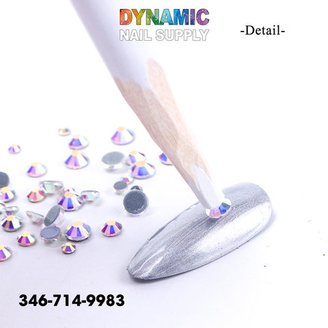 The image showcases a metallic silver nail being decorated with small, round rhinestone crystal gems. A QHTR360 Wooden Nail Dotting Pencil is used to precisely apply a single gem while others are scattered around the scene. The image also features the text "Dynamic Nail Supply" along with the phone number: 346-714-9983.