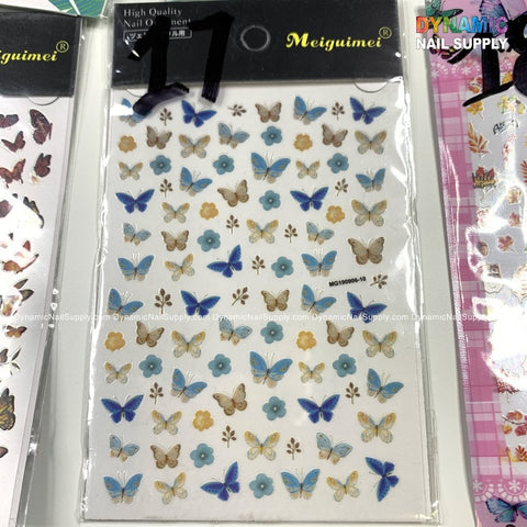 A display featuring "Butterfly stickers for nails art design" from Dynamic Nail Supply showcases exquisite nail art. These high-quality stickers include a variety of designs, such as blue and brown butterfly motifs and blue flowers on a white background. The packaging prominently features the label “High Quality Nail” and is surrounded by similar nail art sticker sheets.