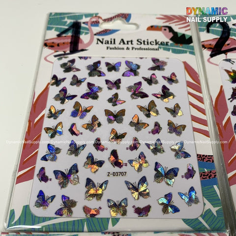 A pack of Butterfly stickers for nails art design - 1 by Dynamic Nail Supply showcases holographic butterfly designs in a variety of sizes. The packaging features the text "Nail Art Sticker" and "Fashion & Professional." Set against a white background, the shimmering butterflies reflect rainbow colors, complemented by tropical-themed graphics.