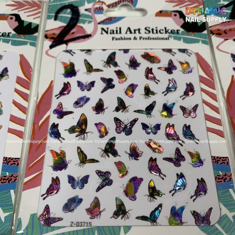 The Butterfly Stickers for Nails Art Design - 2 from Dynamic Nail Supply are showcased on packaging adorned with vibrant holographic butterfly illustrations of different sizes and arrangements. The background features abstract motifs with flamingos and tropical leaves, along with the labels "Dynamic Nail Supply" and "Fashion & Professional.