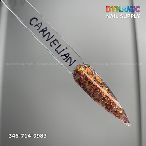 A color sample nail tip labeled Carnelian #330 - Acrylic Glitter Powder exhibits a dazzling blend of reddish-orange and gold glitter, ideal for enduring nail art. The vibrant hue stands out against the neutral gray background. At the top right is the text Dynamic Nail Supply, and at the bottom is 346-714-9983.