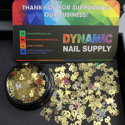 A card displaying the contact information for Dynamic Nail Supply, adorned with a vibrant geometric design, is positioned above a container of "Christmas Metal Sequins for Nail Art Designs." These stunning decorations feature stars, hearts, and flowers elegantly arranged on a black surface.