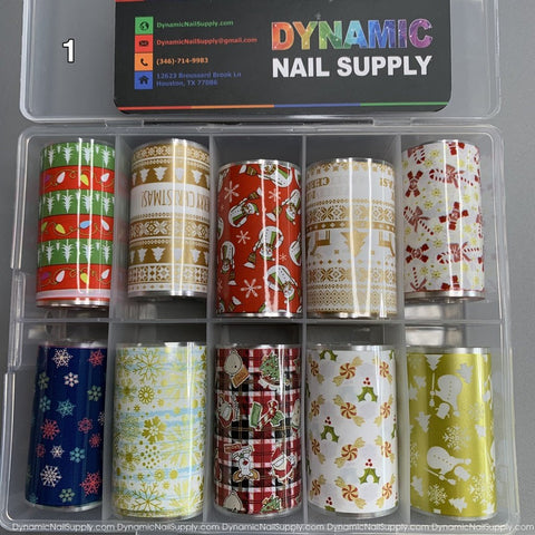 A festive box containing the Christmas Nail Art Foils - [01] from Dynamic Nail Supply showcases a variety of holiday-themed designs, including Christmas trees, snowflakes, reindeer, and candy canes in vibrant shades of red, green, gold, and white. At the top inside the box is a contact card from Dynamic Nail Supply.