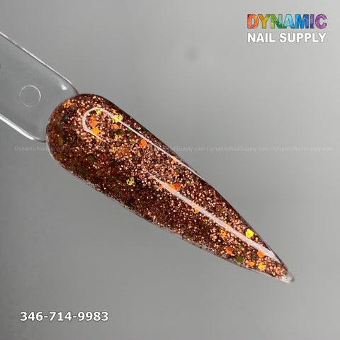 A close-up showcases a long, pointed nail sample on a transparent stick, featuring the Copper acrylic glitter powder with its glittery bronze hue and orange and gold flecks. The background is gray. Dynamic Nail Supply is displayed in colorful text at the top right, while 346-714-9983 is at the bottom left—an ideal choice for those searching for long-lasting nails.