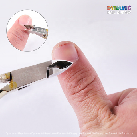A close-up of a hand using the D501 Professional Stainless Steel Cuticle Nipper to trim a fingernail, with the precision cut highlighted in a magnified inset. Dynamic Nail Supply's branding appears at both the top right and bottom edge, emphasizing their premium manicure tools for flawless grooming.