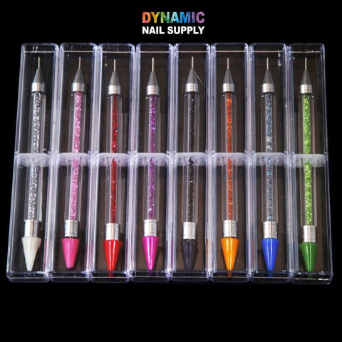 A set of ten Dual-head Rhinestone Picker Pens from Dynamic Nail Supply is showcased in a transparent plastic case. The tools feature handles in a variety of colors embedded with rhinestones, including white, pink, red, purple, black, orange, and blue. The case rests against a black background with the Dynamic Nail Supply logo at the top.