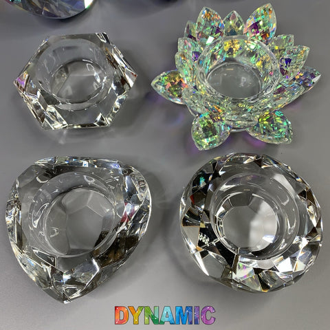 Displayed against a gray background are four lead crystal dappen dishes from Dynamic Nail Supply. Each dish features distinct geometric designs including hexagon, round, heart, and lotus shapes, all with a rainbow-reflective surface. The word "DYNAMIC" is boldly printed in colorful letters beneath them.