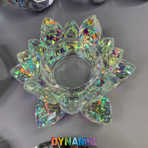 A lotus-shaped lead crystal dappen dish with iridescent petals from Dynamic Nail Supply reflects colorful light patterns. Below it, the word DYNAMIC is artistically displayed in rainbow-colored block letters on a gray surface.