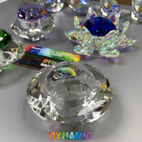 A display of Dynamic Nail Supply's CRYSTAL DAPPEN DISH in a lotus shape showcases faceted lead crystal tealight holders in clear, green, and iridescent blue hues. A business card is subtly positioned in the background, while "Dynamic" is vividly highlighted at the bottom of the image.