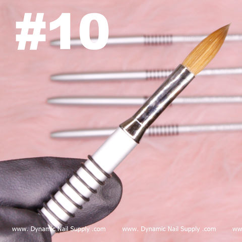 A close-up shot features a Dynamic® High-quality 3D Brush (Kolinsky hair) in size #10, held by a gloved hand. The metallic handle and precisely pointed bristles are prominently displayed. In the background, slightly out of focus, four professional brushes are neatly arranged. Text at the bottom reads “Dynamic Nail Supply.” The surface appears as a pink, textured backdrop.