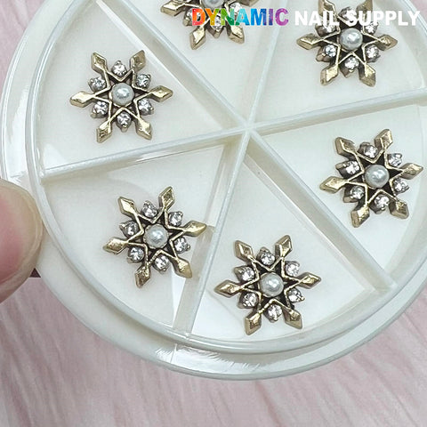 Close-up of the Antique Star Flowers Snowflake Charm for Nails Art Designer by Dynamic Nail Supply, showcasing six compartments within a circular nail art wheel. Each compartment is filled with metallic star-shaped embellishments that resemble antique snowflakes, featuring a central pearl surrounded by small gems and gold points in an intricate starburst pattern.
