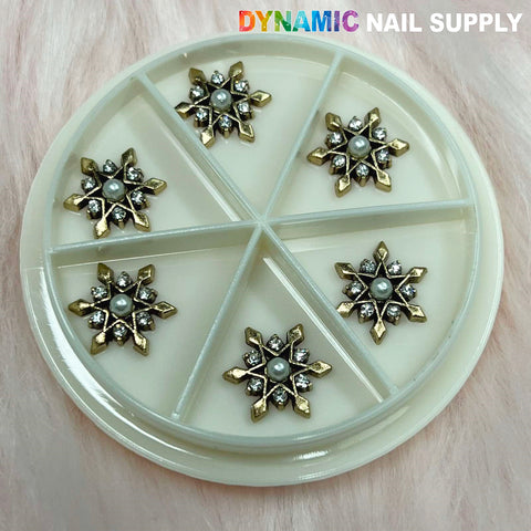 A circular container with six compartments, each containing a decorative charm for nails. These Antique Star Flowers Snowflake Charms feature star shapes with gold and silver accents, a central pearl, and small rhinestones. The brand name "Dynamic Nail Supply" is prominently displayed at the top in colorful text.