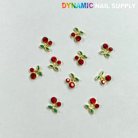 The 10 pcs Small Red Cherry Charms for Nails Art Designer feature red gem berries and gold stems, accented with green gem leaves, scattered elegantly on a light background. The Dynamic Nail Supply brand name is prominently displayed in the top right corner, making them a perfect addition to elevate your nail art.
