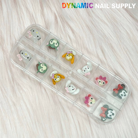 The Cartoon Characters Nail Charms set 01 by Dynamic Nail Supply is a clear plastic container with a lid that houses twelve charming cartoon-style nail charms. The designs feature pastel-colored animals such as bears, penguins, and possibly frogs. Each compartment displays a small 3D figure on a pink fuzzy background.